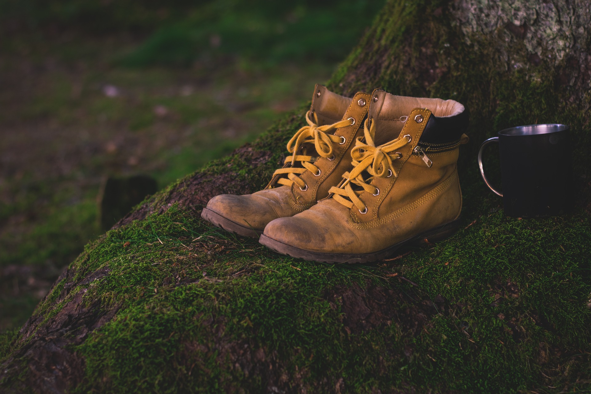 A pair of yellow hiking boots next to a black mug